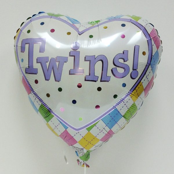 Inflated heart shaped foil balloon with white center with multi-colored polka dots that says "Twins!" in purple serif font and multi-colored argyle patterned border.